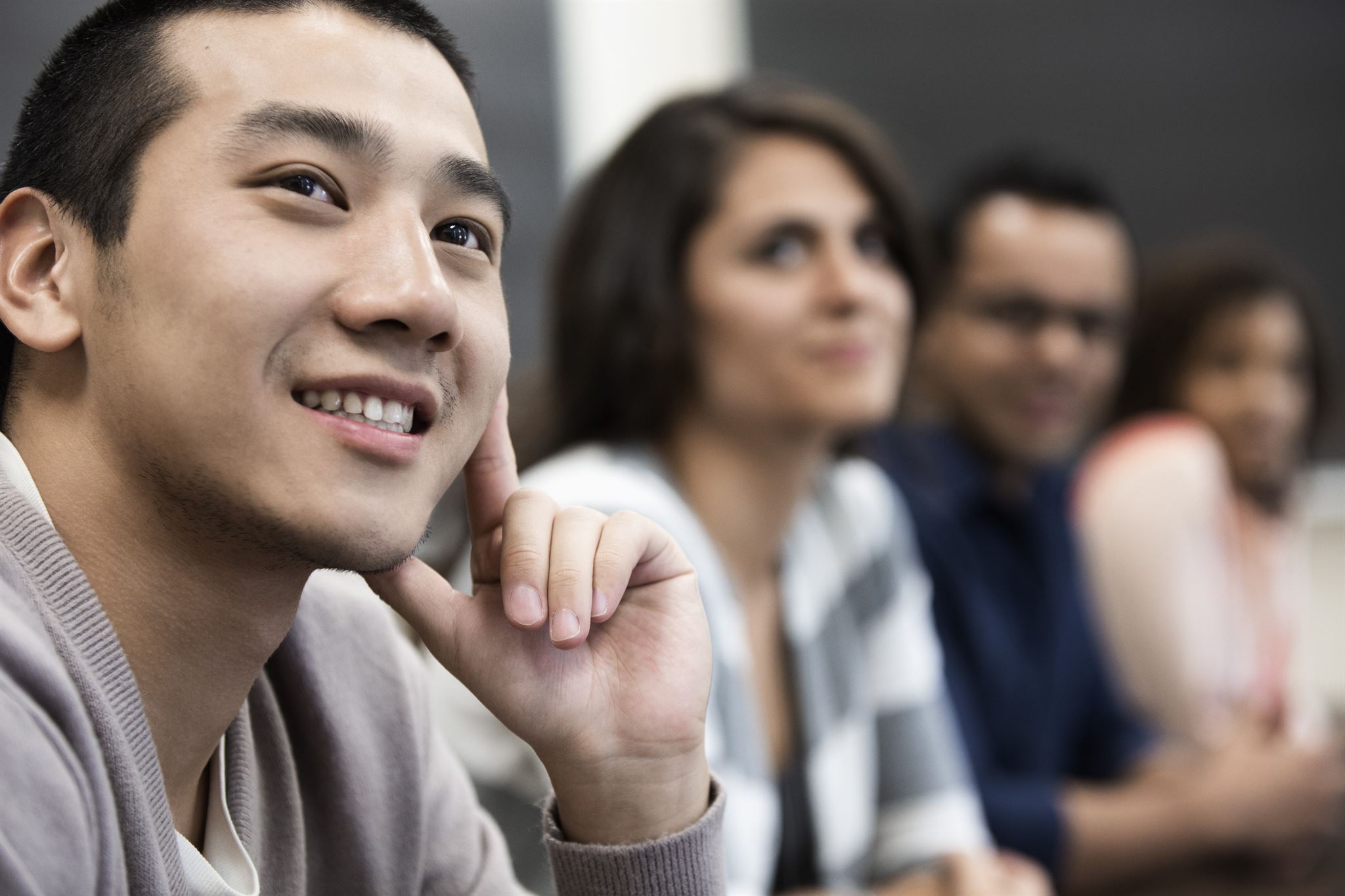 Smiling-young-man-in-focus-seated-with-three-other-people-out-of-focus